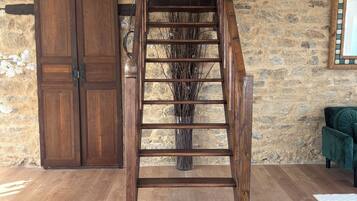 A wooden staircase leading to a loft area with a stone wall and a green upholstered chair.