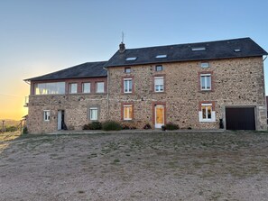 A two-story stone building with a gravel driveway and a small garden area.