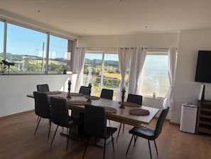 En matplats med ett stort bord, stolar och utsikt över ett landskap genom stora fönster.