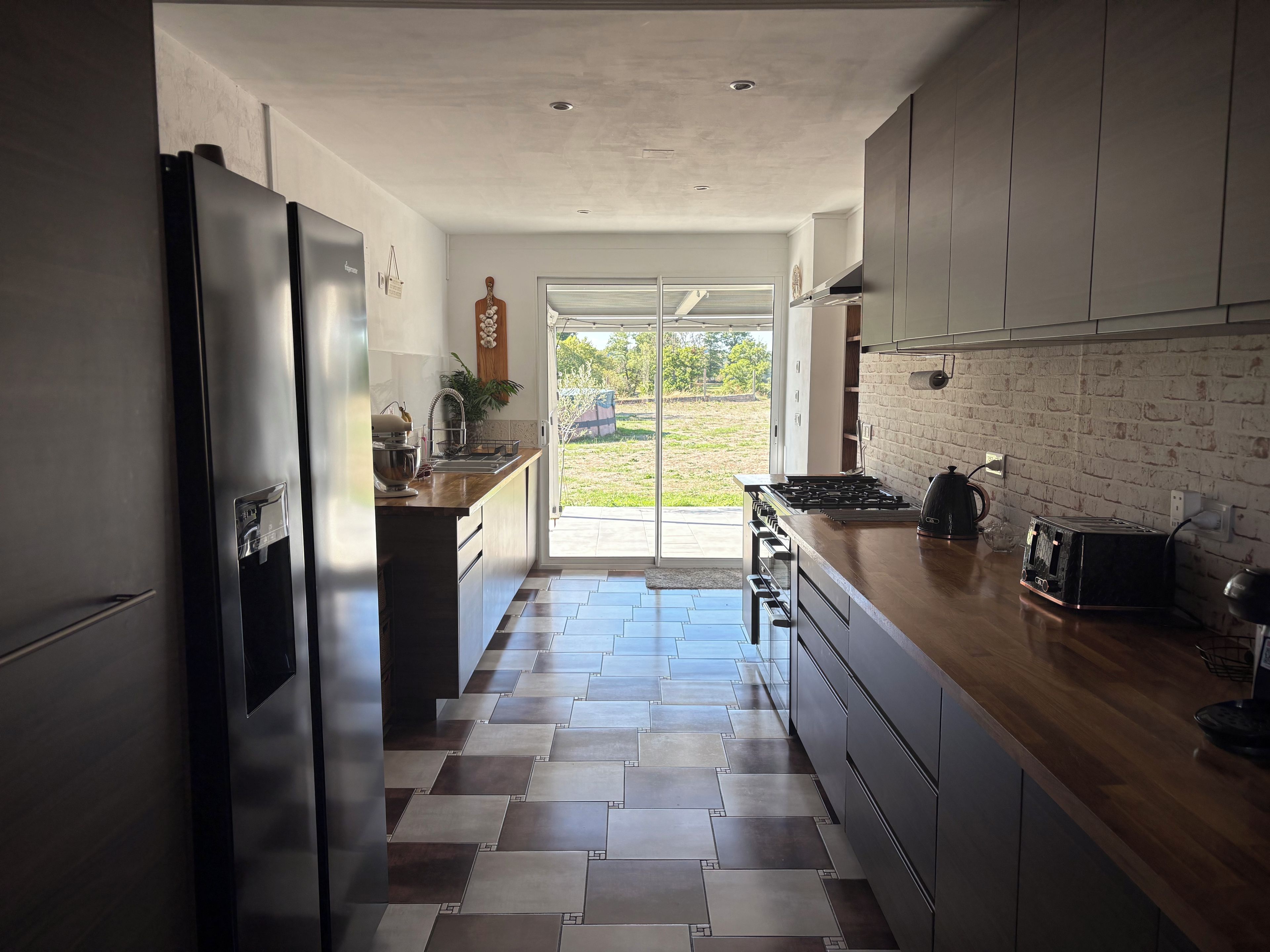 A modern kitchen with a central island, stainless steel appliances, and a view to the outside.
