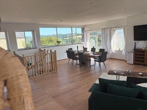 A spacious living area with a dining table, chairs, a green sofa, and a TV.