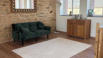 Une pièce avec un mur en pierre, un canapé vert, un tapis blanc, un plancher en bois, un meuble en bois et une fenêtre donnant sur un beau paysage.