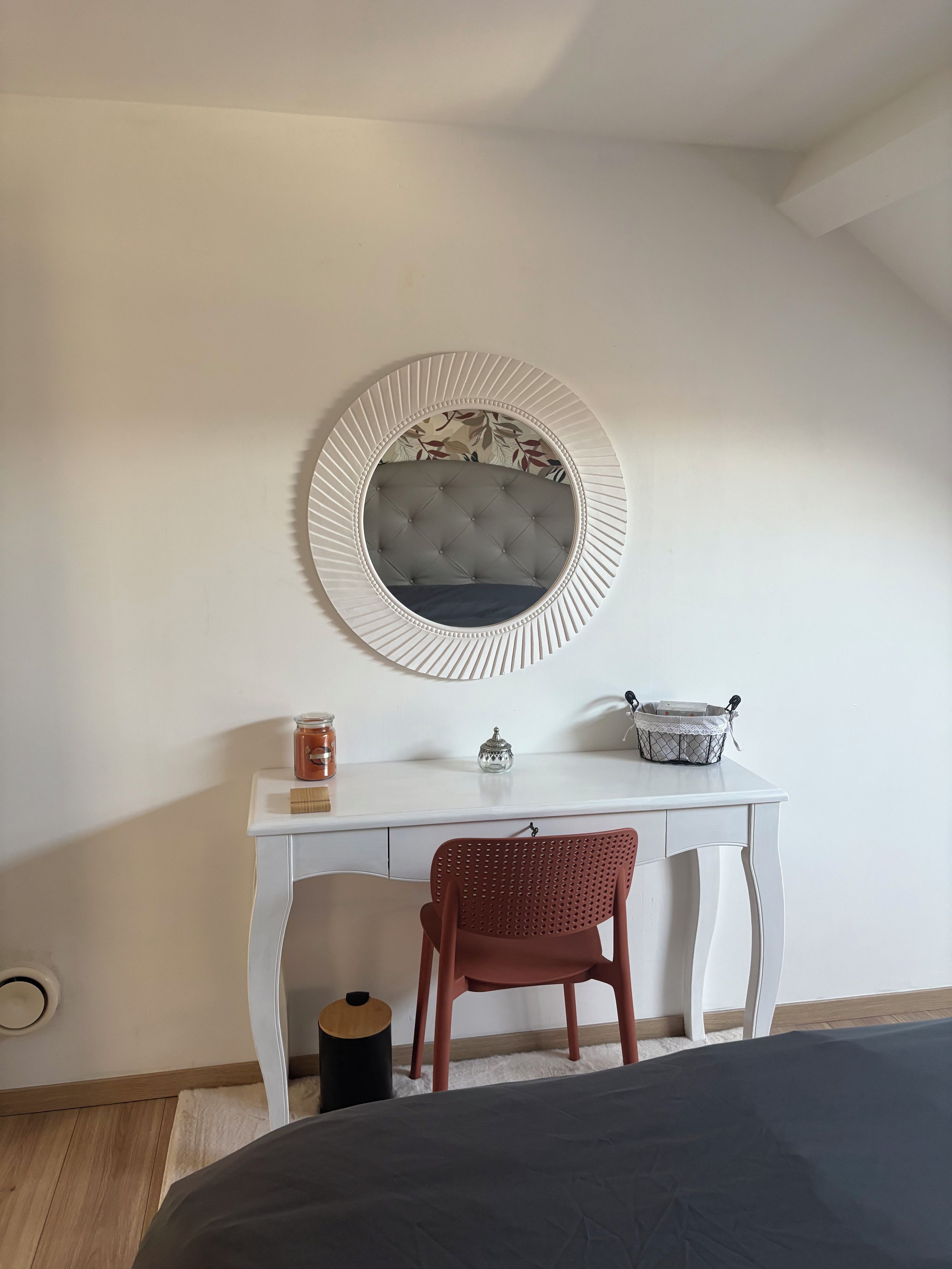 Une chambre à coucher avec un lit, un bureau blanc doté d’un miroir, une chaise rouge et une petite table ronde sur laquelle sont posés divers objets.