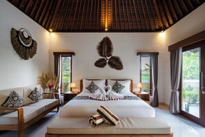 A hotel room with a large bed, a sofa, two nightstands, decorative wall art, and a view of greenery through the windows. - Wonderful bed & breakfast with 1 bedroom and Private Pool in Sebatu (Sebatu)