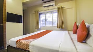 A hotel room with a bed, a window with curtains, an air conditioning unit, and a wall-mounted television.