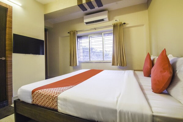 A hotel room with a bed, a window with curtains, an air conditioning unit, and a wall-mounted television.