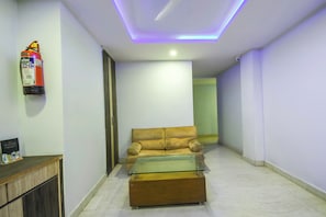 A hallway with a sofa and a glass-top coffee table, a fire extinguisher on the wall, and a door leading to another room.