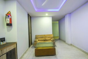 A hallway with a sofa and a glass-top coffee table, a fire extinguisher on the wall, and a door leading to another room.