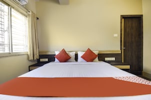 Una habitación de hotel con una cama grande, dos mesitas de noche, un cabecero de madera, una puerta y una ventana con cortinas.
