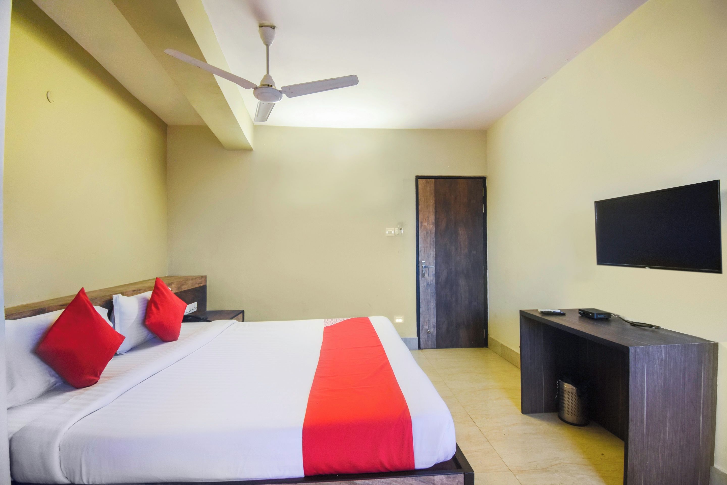 A hotel room with a bed, a desk, a television, and a ceiling fan.