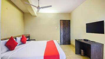 A hotel room with a bed, a desk, a television, and a ceiling fan.