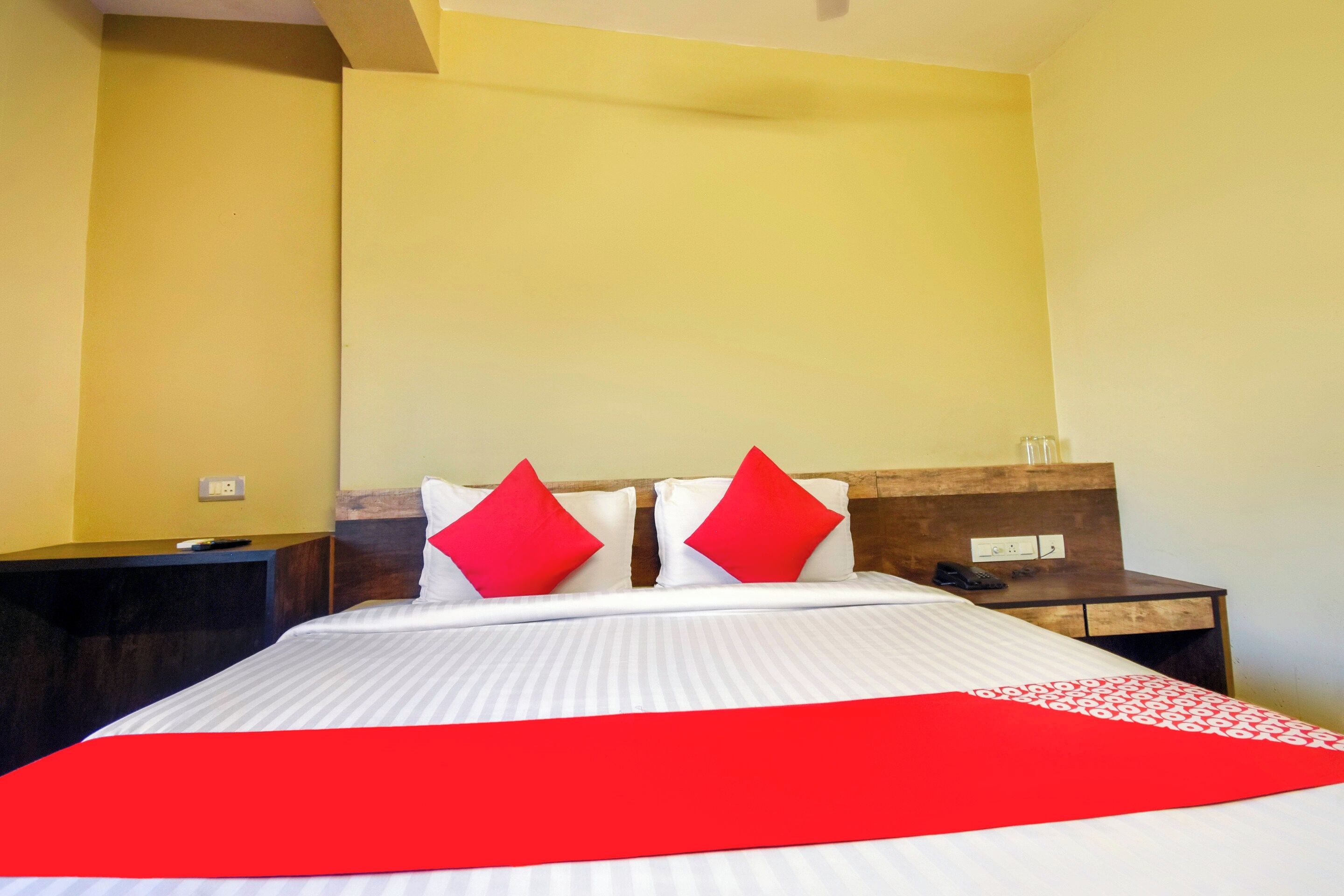 A hotel room with a bed, two red pillows, a bedside table with a phone, and a nightstand.