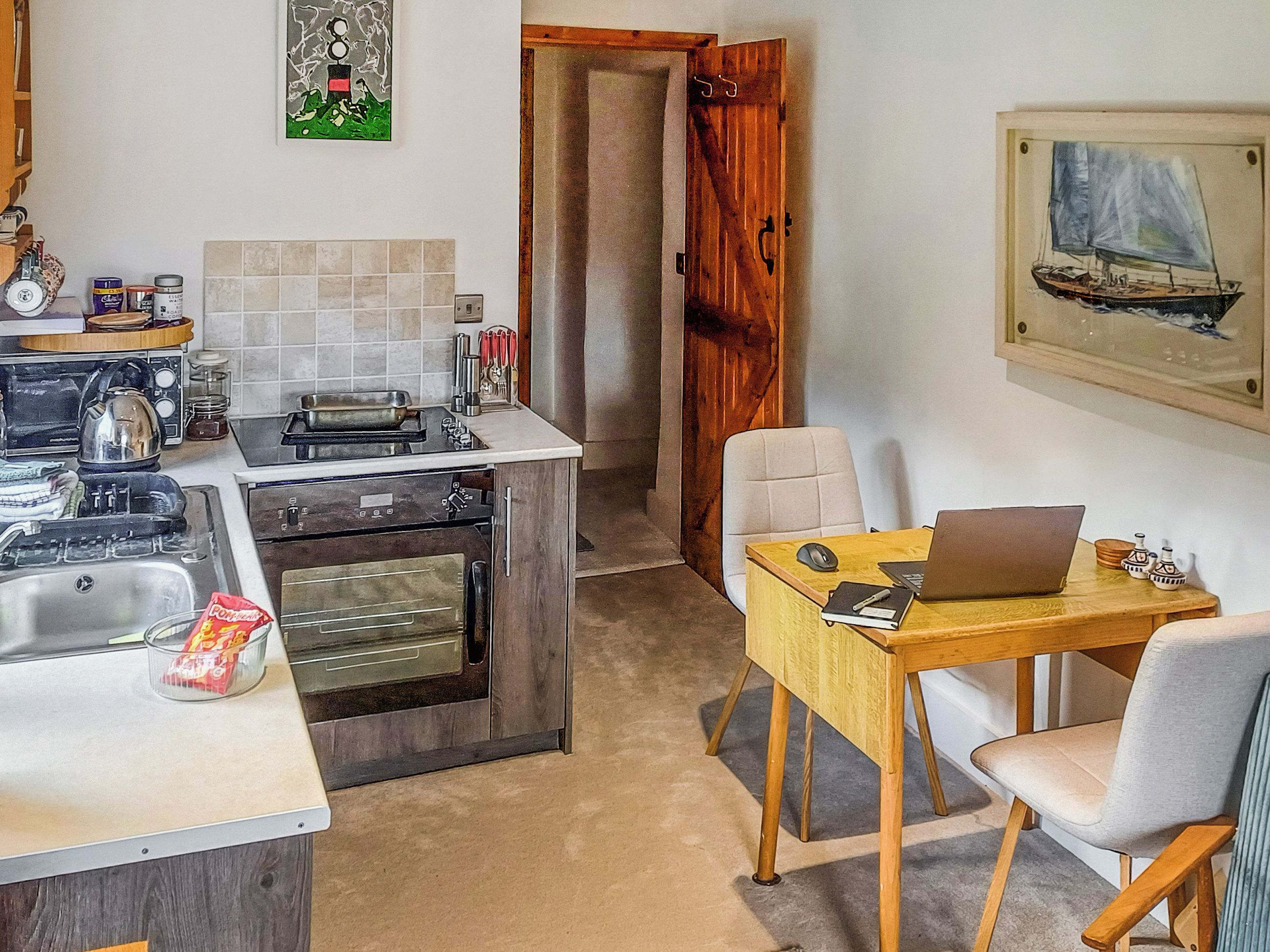 Une cuisine compacte équipée d’une cuisinière, d’un four et d’un évier, un coin repas avec une table et une chaise, et une porte donnant sur une autre pièce.