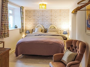 A bedroom with a large bed, two bedside lamps, a chair, and a patterned wallpaper. - South Nethercott Farm Annexe (Okehampton - Whiddon Down)