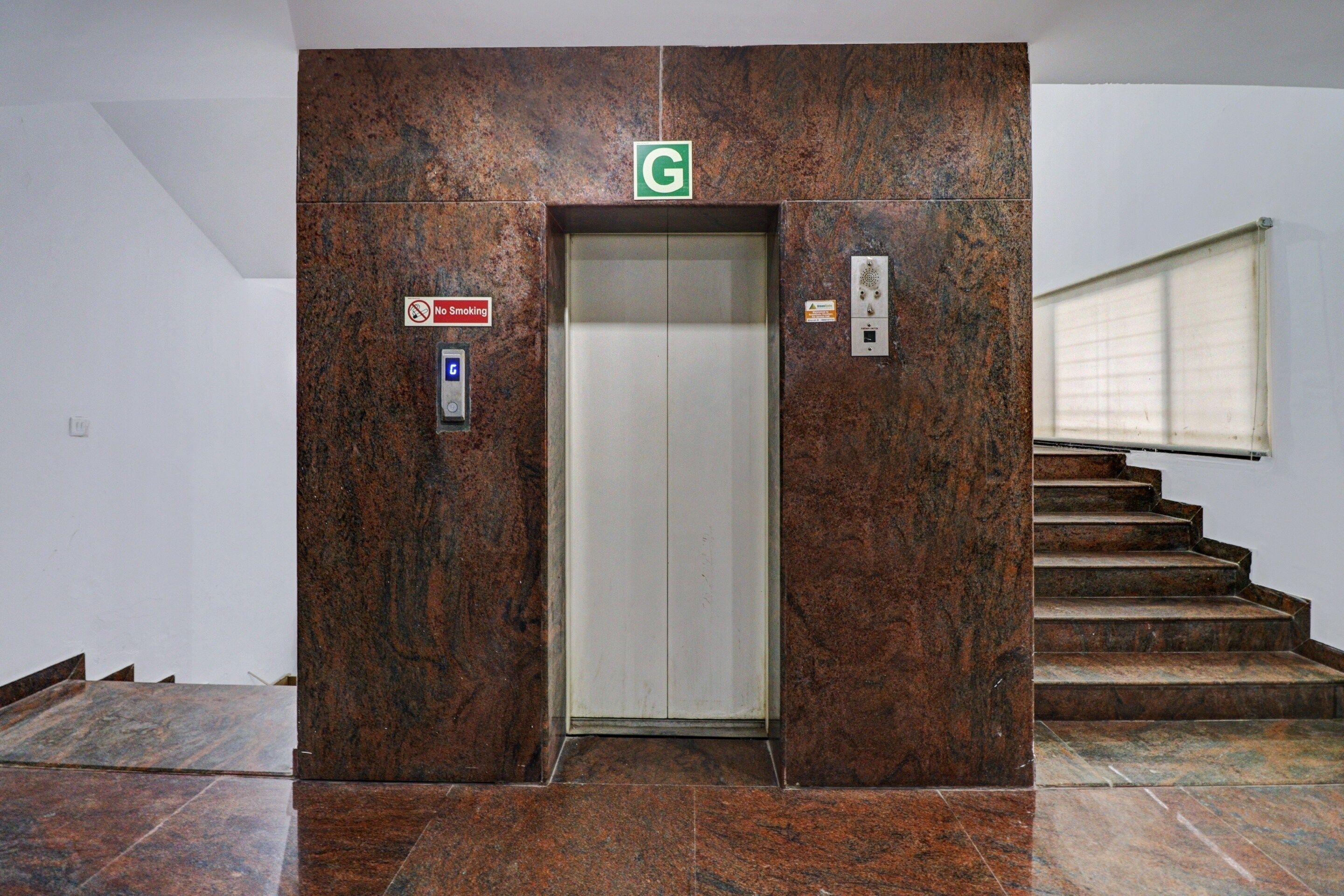 An elevator with a 'No Smoking' sign, a green 'G' sign above it, and a control panel on the right.
