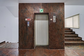 Un ascensor con un cartel de 'No Fumar', una señal verde con la letra 'G' arriba y un panel de control a la derecha.