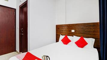 A hotel room with a wooden headboard, white bedding, red pillows, and a breakfast tray with a kettle.