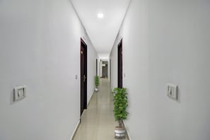 A corridor with doors on both sides, a potted plant in the center, and light switches on the walls. - Hotel O Pride Inn (Bangalore)