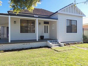 A two-story house with a covered porch, large windows, and a brick foundation. - Breeze on Prince: Spacious cottage offering modern comfort (Waratah)