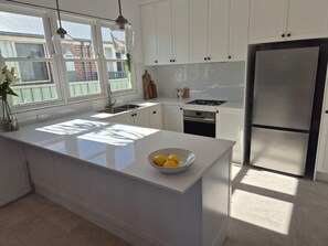 A modern kitchen with white cabinetry, a stainless steel refrigerator, and a large island with a bowl of lemons. - Breeze on Prince: Spacious cottage offering modern comfort (Waratah)