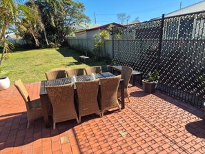 An outdoor patio with wicker furniture and a brick floor. - Breeze on Prince: Spacious cottage offering modern comfort (Waratah)