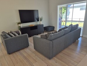 A modern living room with a grey sofa set, a flat-screen TV mounted on a black console, and a sliding glass door leading to an outdoor area. - Spacious home 'Breeze on Prince', offers modern connectivity and luxury comfort. (Waratah)
