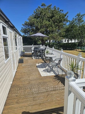 A wooden deck with outdoor furniture, a white railing, and a tree in the background. - Greenacres Holiday Park - Holiday Accommodation 20263 (Porthmadog)