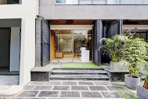 A building entrance with a glass door, a set of stone steps, and a small green area. - Townhouse Sector 51 Gurgaon (Gurugram)