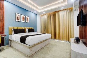 Una habitación de hotel con cama, televisor, cafetera y un amplio ventanal con cortinas.