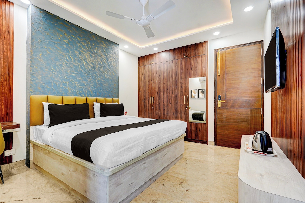 Habitación de hotel con cama, armario de madera, escritorio con hervidor y ventilador de techo.