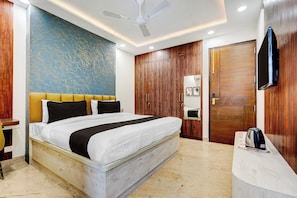 Habitación de hotel con cama, armario de madera, escritorio con hervidor y ventilador de techo.