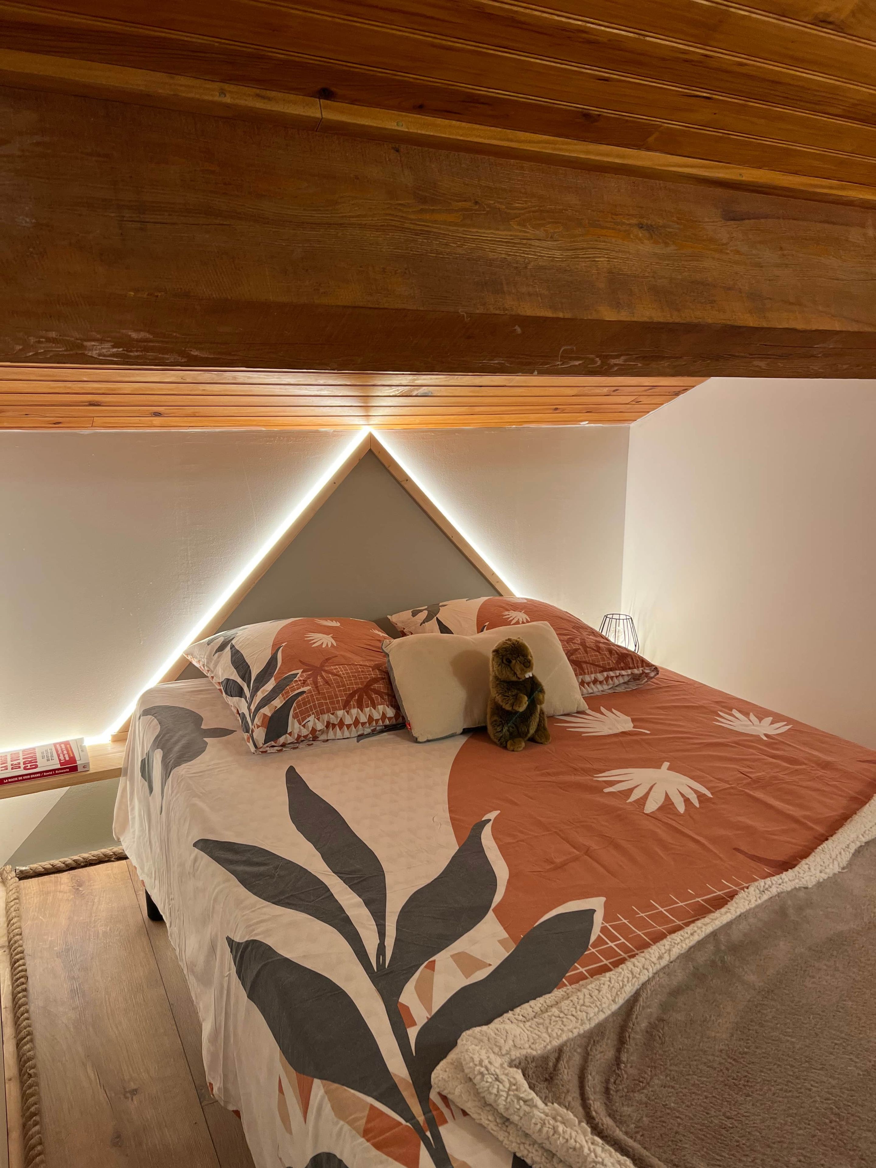 Ein Schlafzimmer mit schrägem Dach, einem Bett mit gemusterten Bettbezügen, Kissen und einem Teddybären.