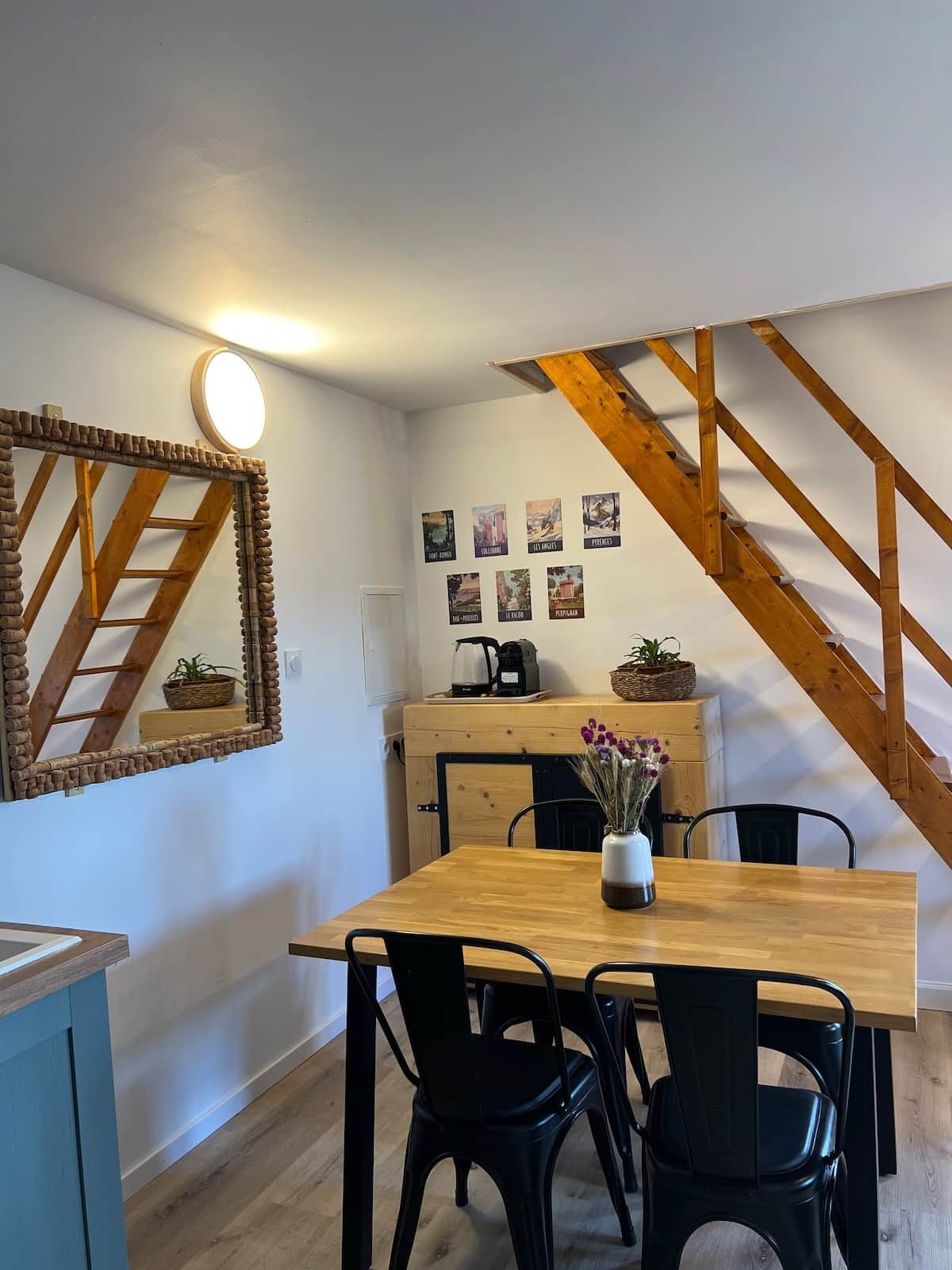 A dining area with a wooden table, black chairs, a mirror with a wooden frame, and a staircase with exposed beams.