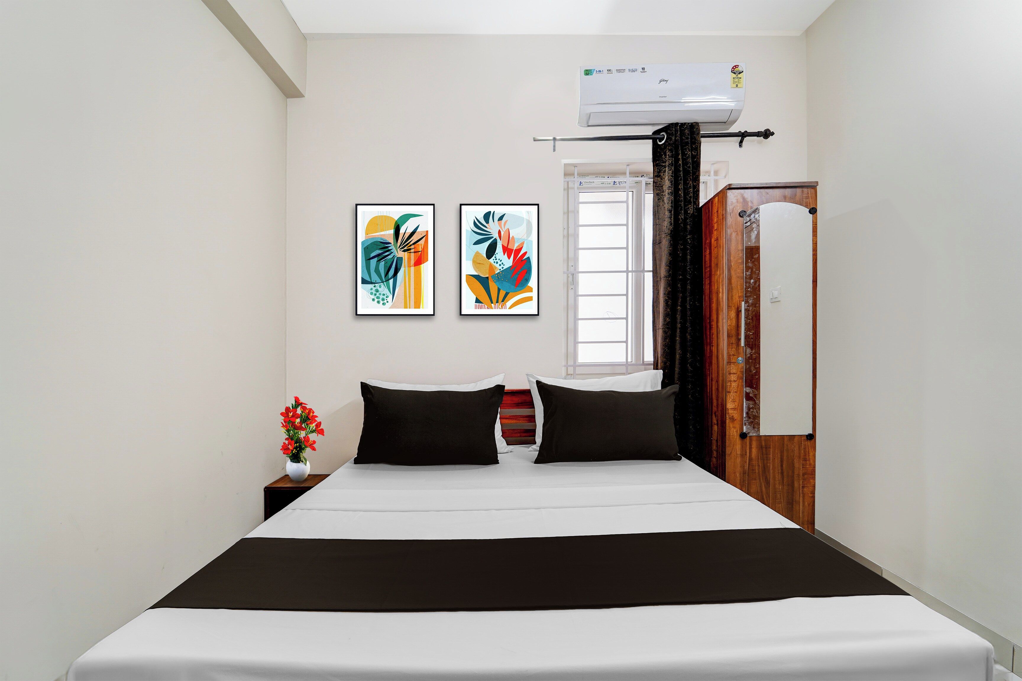 Habitación de hotel con una cama, dos obras de arte colgadas en la pared, una ventana y un equipo de aire acondicionado.
