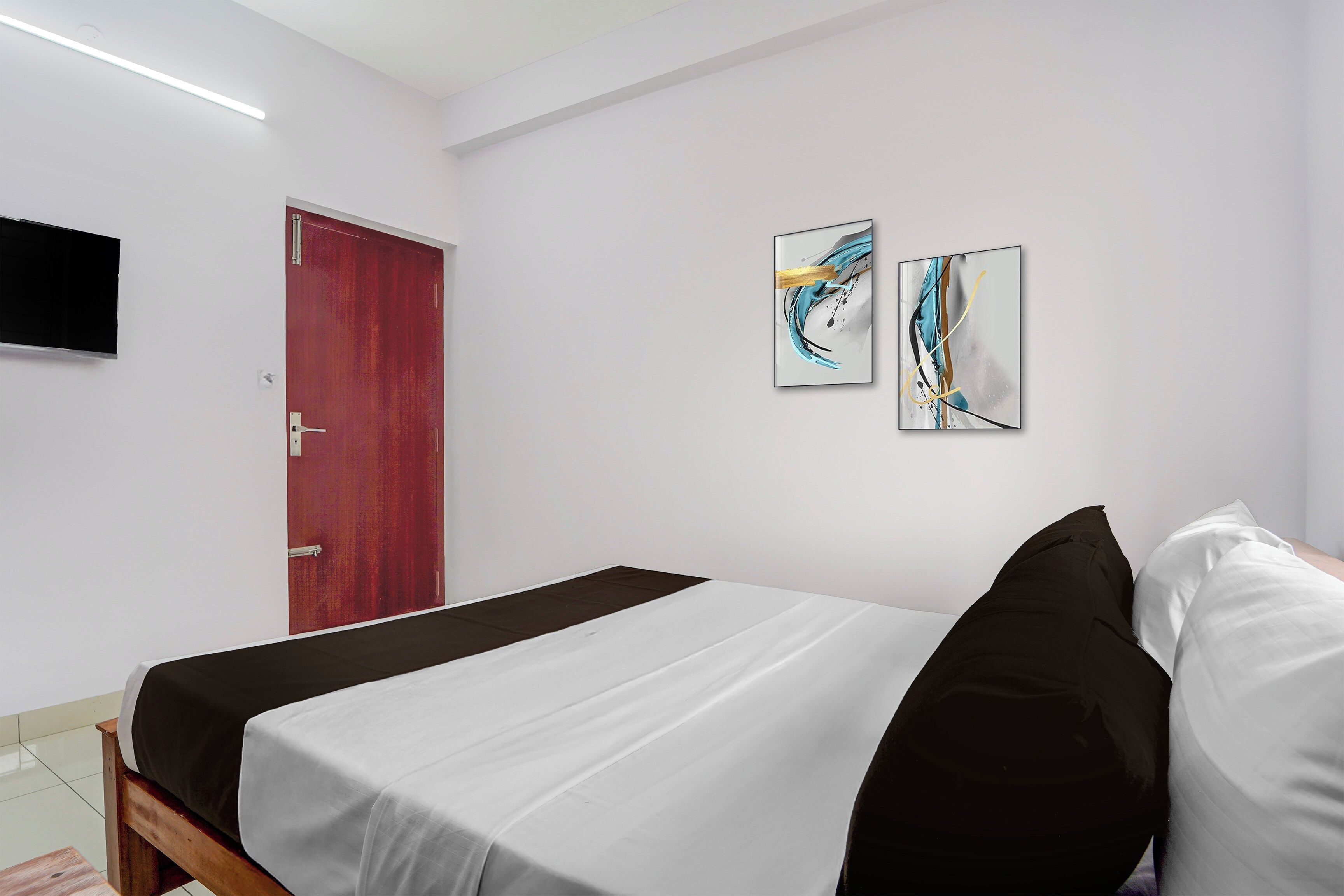 A hotel room with a bed, a red door, and two abstract paintings on the wall.
