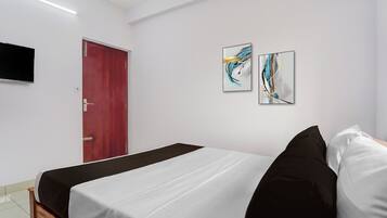 A hotel room with a bed, a red door, and two abstract paintings on the wall.