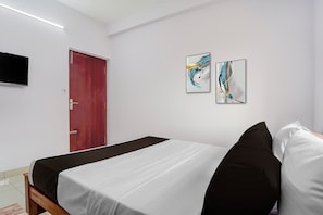 A hotel room with a bed, a red door, and two abstract paintings on the wall.