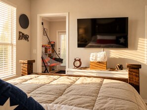 A bedroom with a bed, a TV mounted on the wall, a clock, and a shelf with items. - Designer Texan Stay - Resort Pool - Arcade & Games (Round Rock)