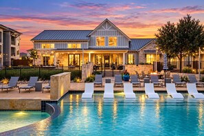 A resort with a swimming pool, lounge chairs, and a building with a stone facade. - Designer Texan Stay - Resort Pool - Arcade & Games (Round Rock)
