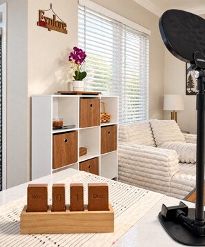 A room with a white bookshelf, a small table with a calendar, and a window with blinds. - Designer Texan Stay - Resort Pool - Arcade & Games (Round Rock)