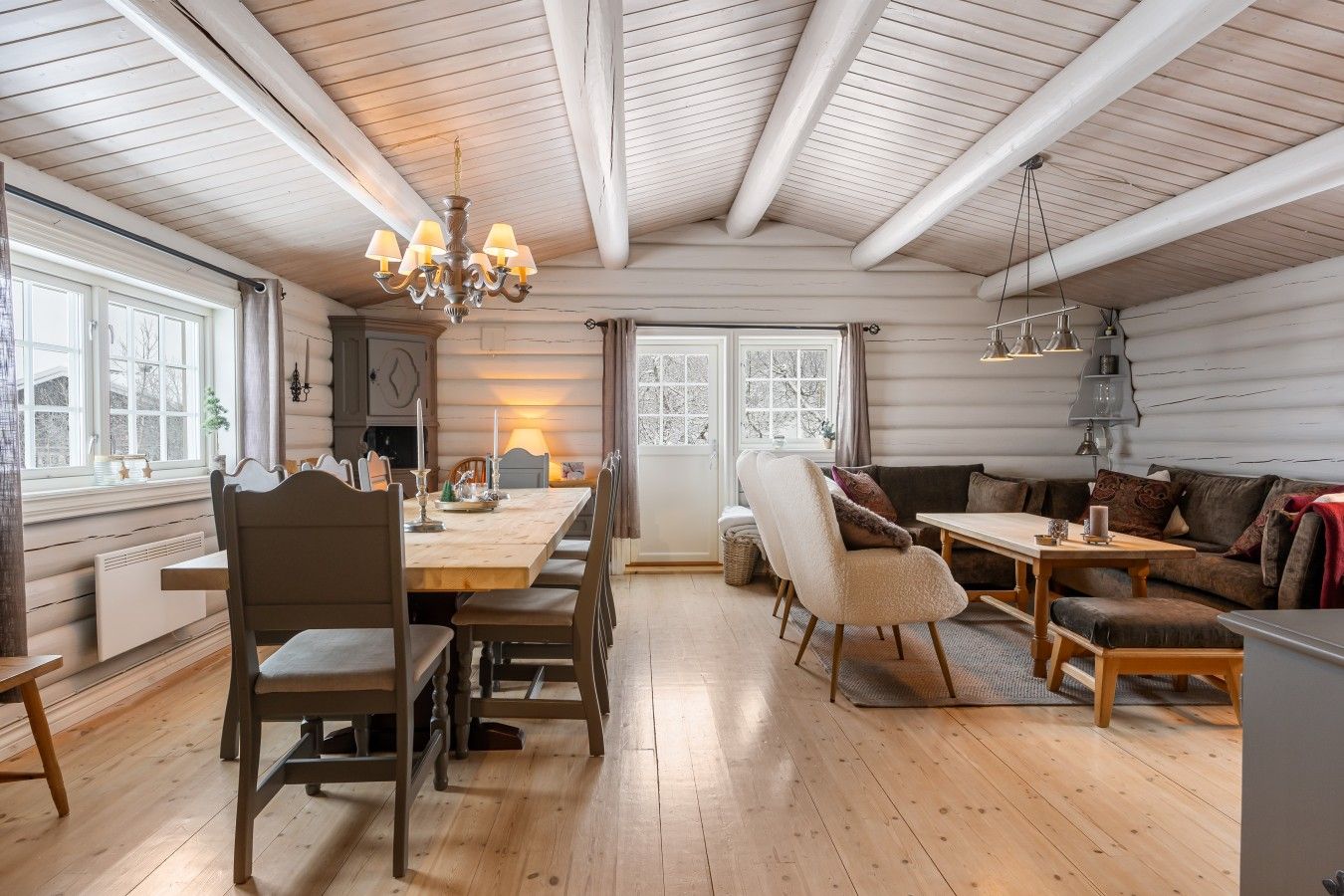 En ombonad inredning med ett matbord i trä, stolar, en soffa och en kristallkrona.