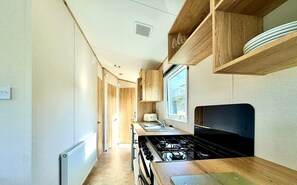 A compact kitchenette with a gas stove, wooden cabinets, and a window providing natural light.