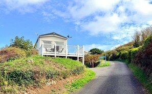Um edifício branco com varanda, um poste de sinalização e uma estrada curvando-se à direita.