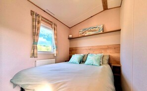 Ein Schlafzimmer mit Bett, einem Fenster mit Vorhängen, einem Bild an der Wand und einer Heizung.