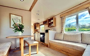 Ein gemütliches Zimmer mit einem Holztisch, einer Bank, einem Sofa und einem Fenster mit Blick auf Grünflächen.
