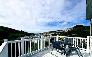 Ein Balkon mit weißer Reling, einem Tisch mit Stühlen und einem Blumenstrauß.