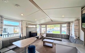 A spacious RV interior with a sofa, a TV, and a dining area. - The Loire - Luxury Retreat by the Sea in Devon (Challaborough)