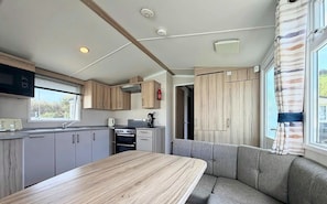 A compact kitchen with a dining area, wooden cabinets, and a window with curtains.