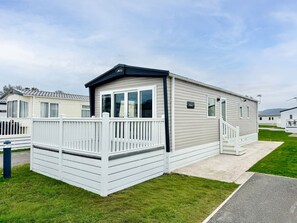 A mobile home with a deck, a covered porch, and a small staircase.