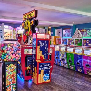 A brightly lit arcade with various gaming machines, including a Pac-Man machine and a claw machine filled with colorful balls. - The Retreat - A Luxurious Caravan in Towyn, Wales (Towyn)